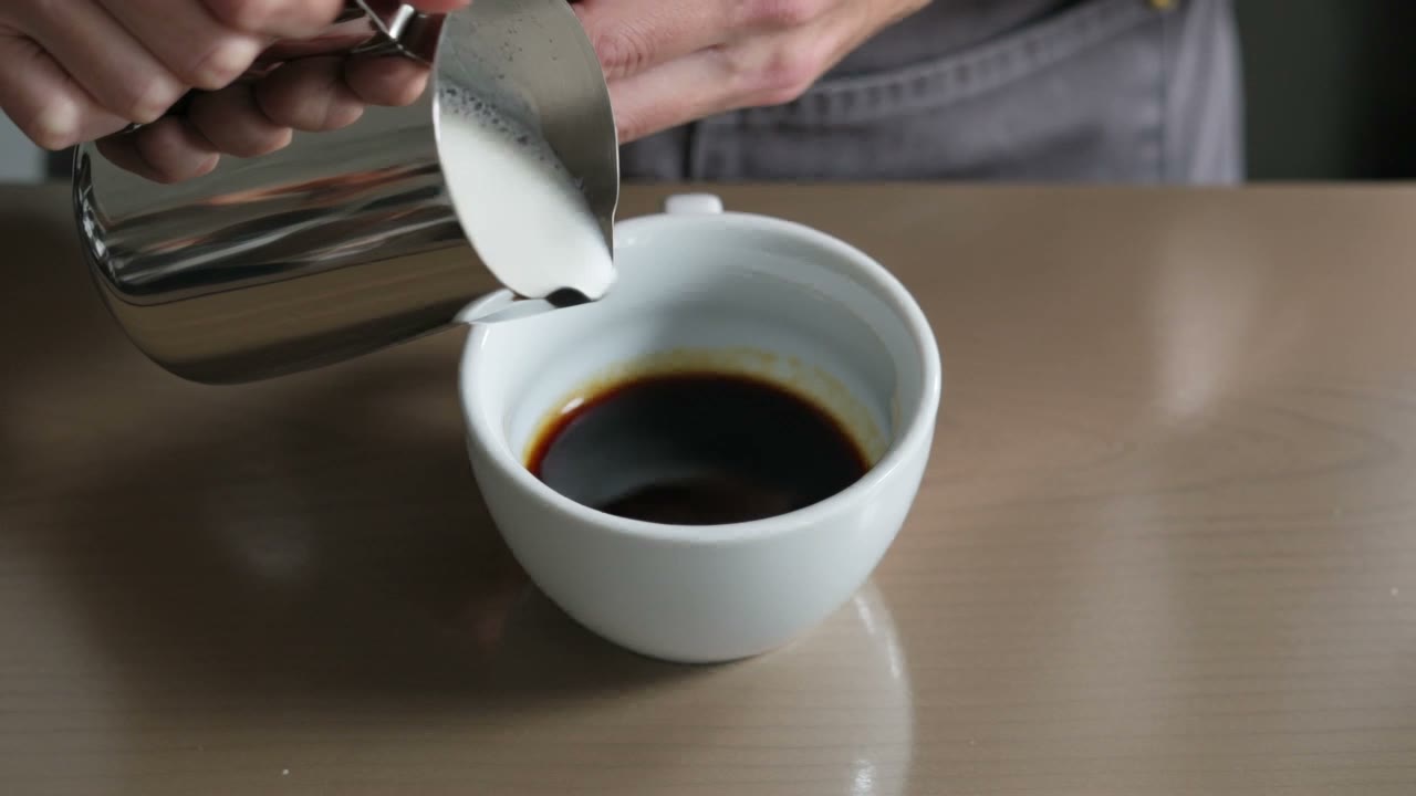 Frame from a Kling V3 video: milk poured into espresso forms a leaf in the foam