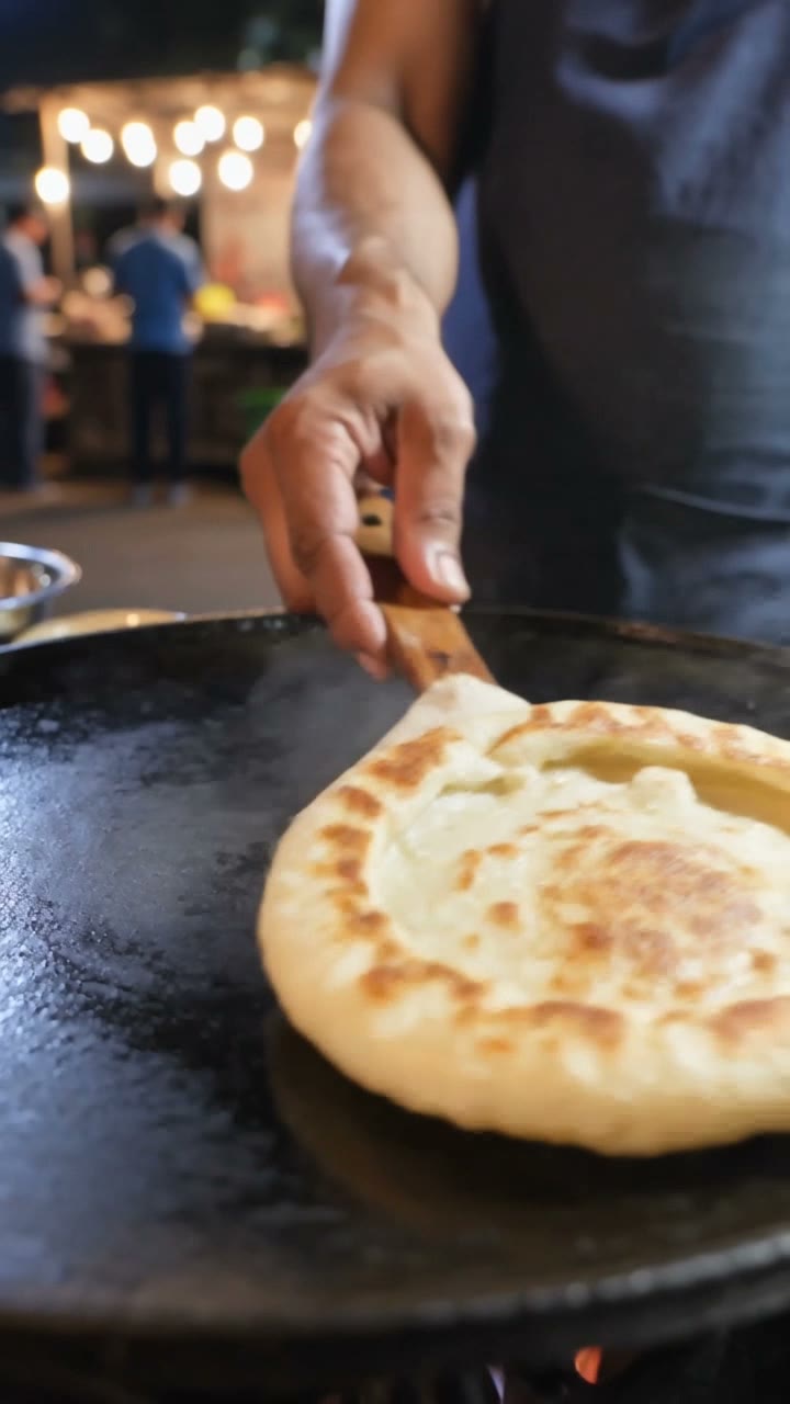Frame from a Kling V3 video: a cook flips a paratha on a street food griddle